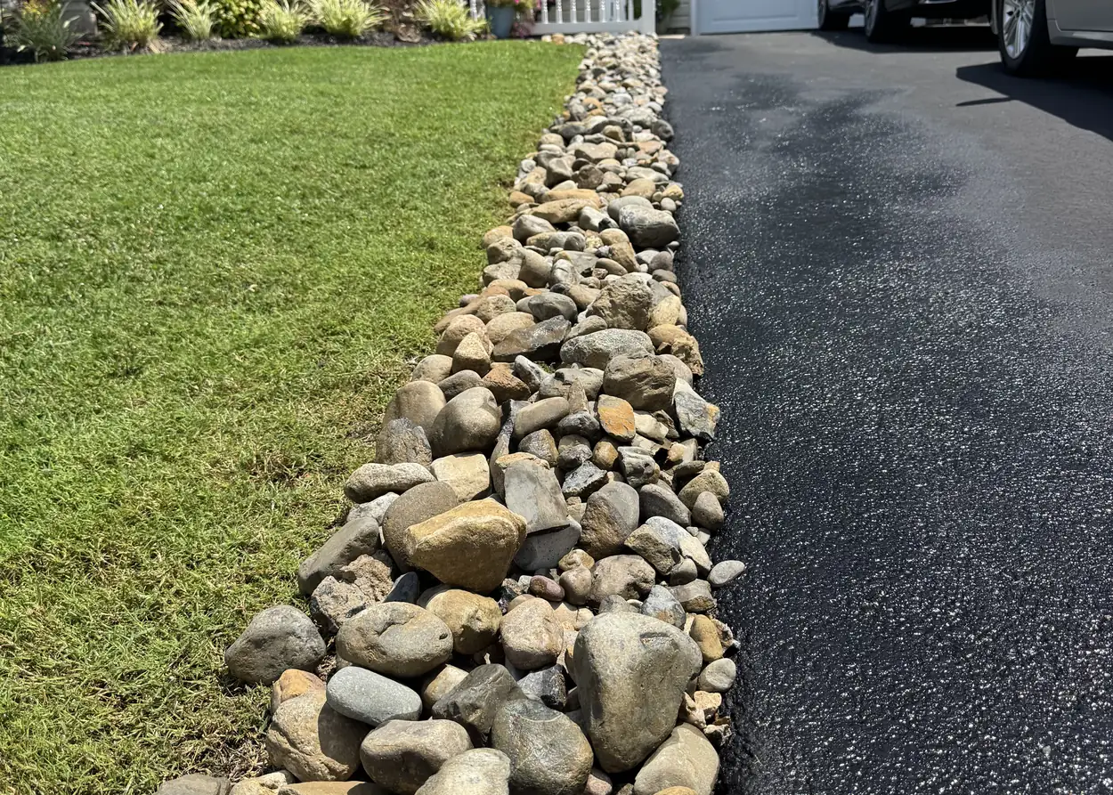 River rock laid in a channel between a lawn and a driveway