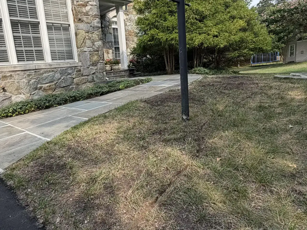 Dry, patchy grass along a flagstone walk beside a stone house