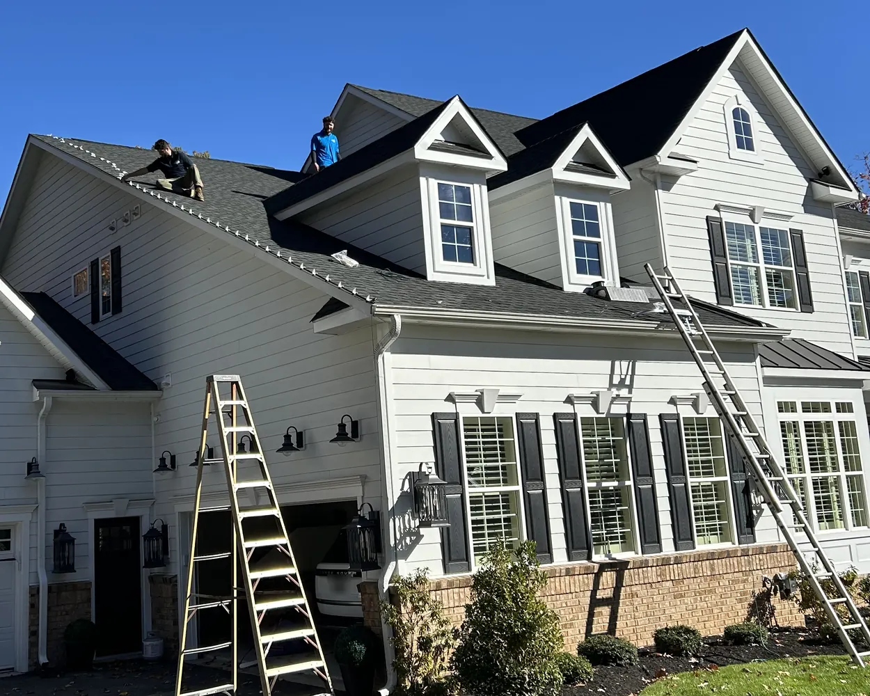 Two of our crew on the roof of a white two-story home, with two ladders up at the front