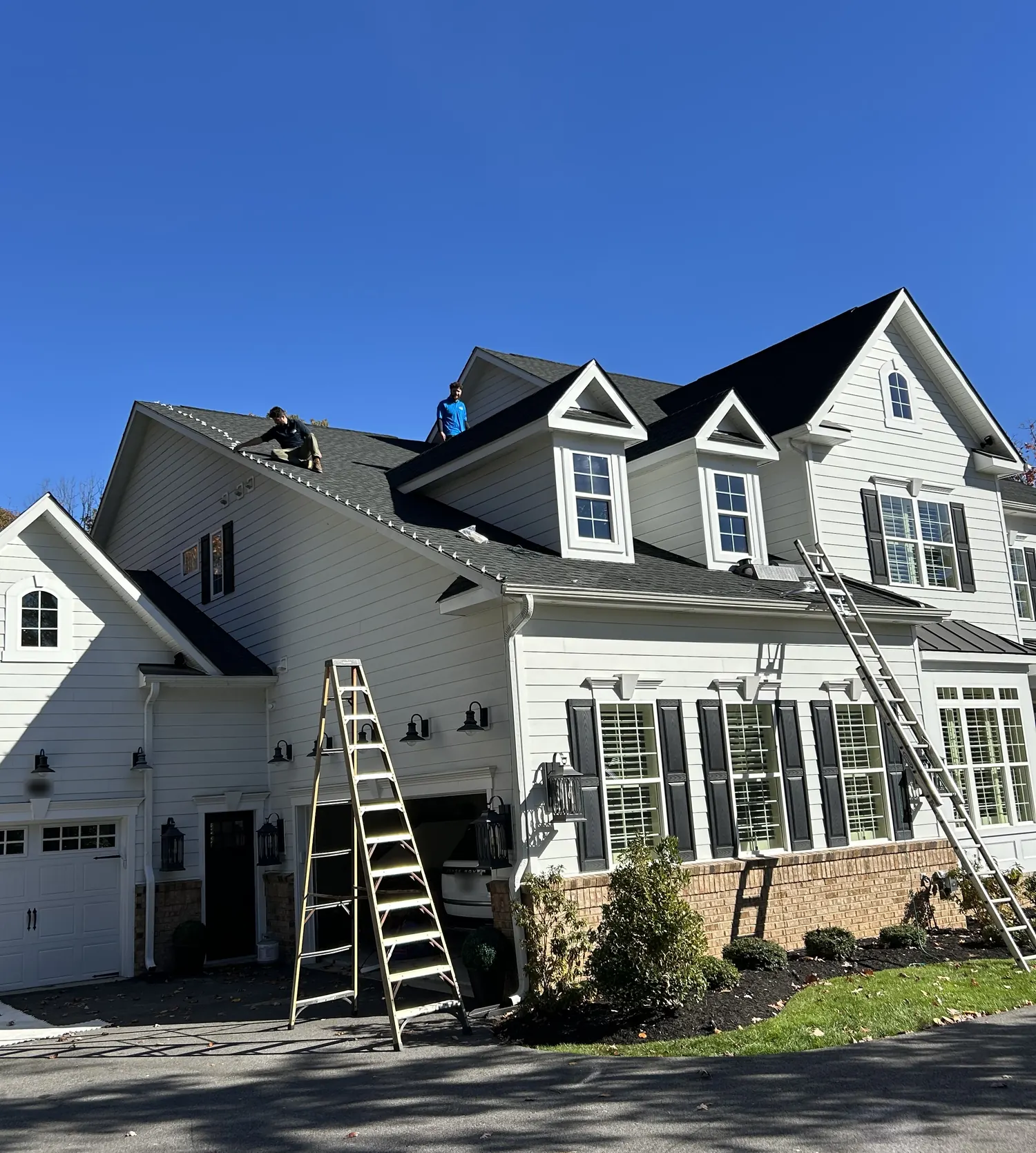 Two Fannon crew members on the roof of a white two-story home, with ladders set up at the front