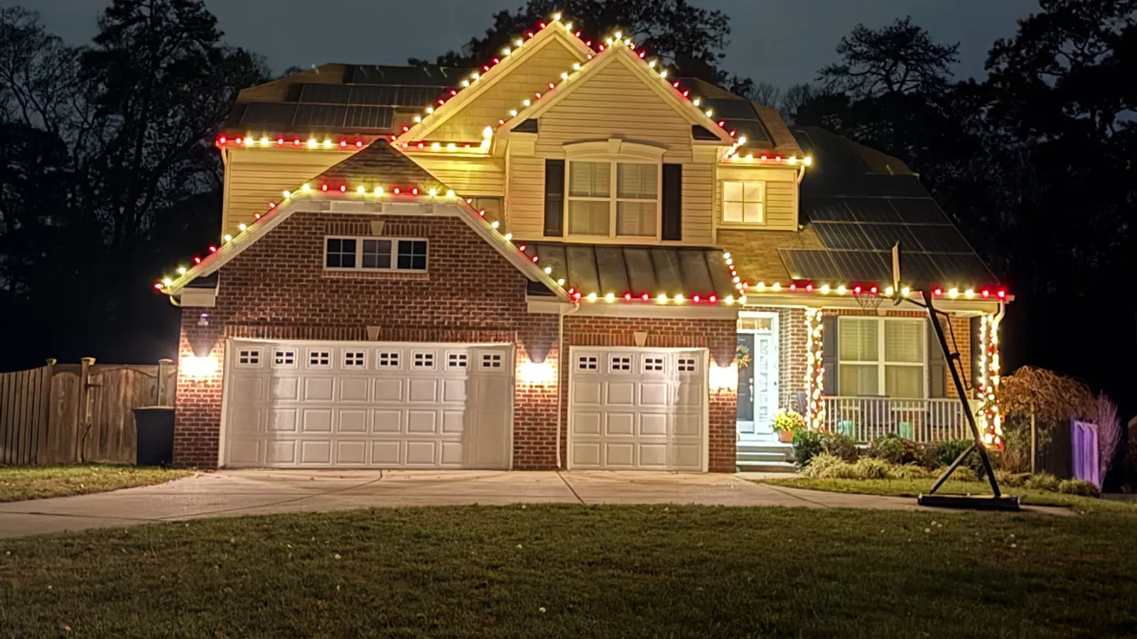 A brick home at dusk with red and warm white lights along every roofline