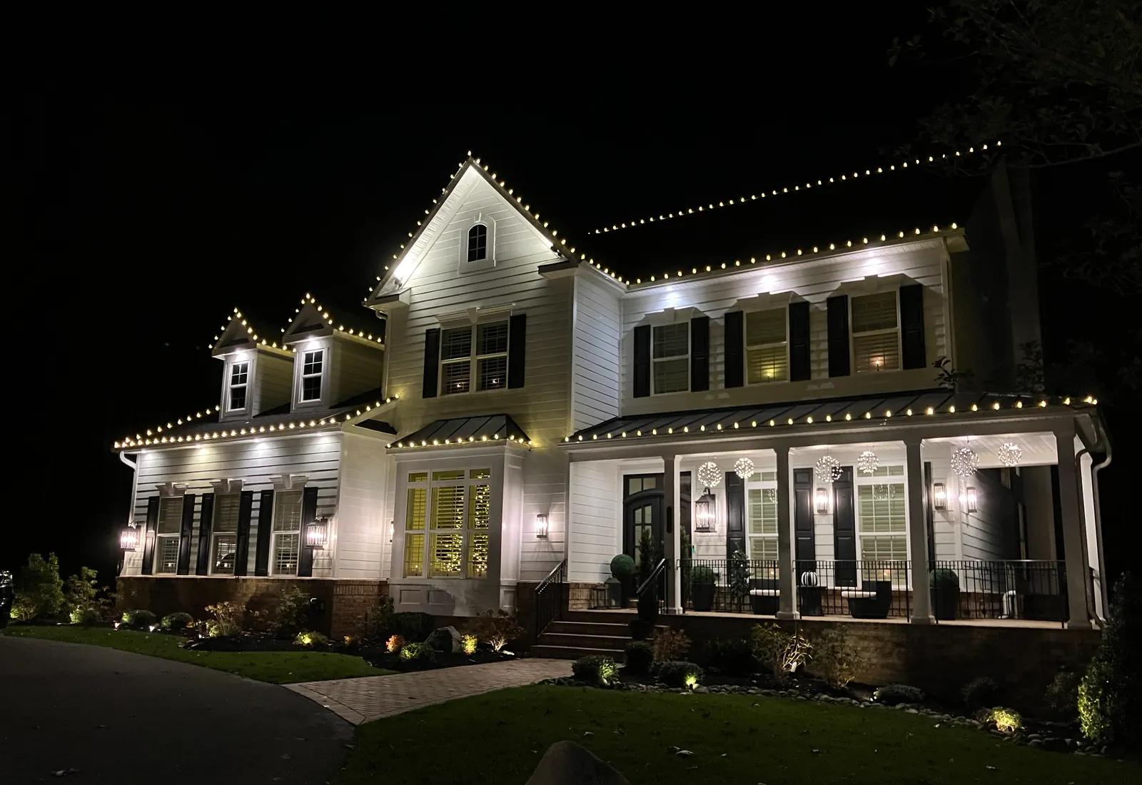 A white colonial at night with warm white lights on every roofline