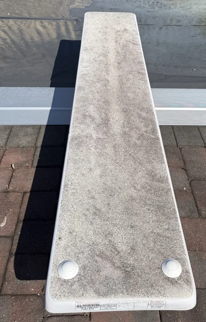 A gray, grimy diving board over brick pavers