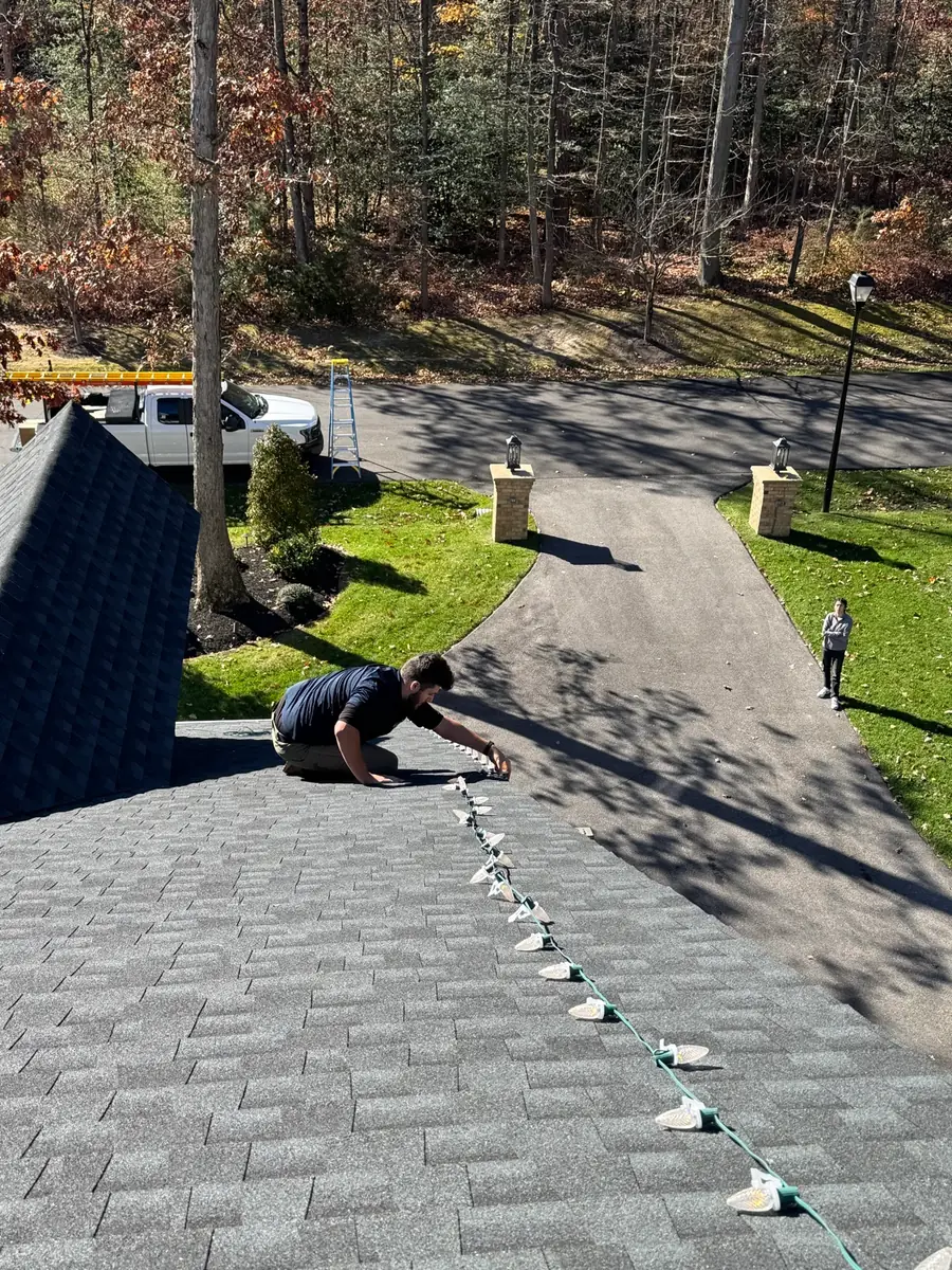 A Fannon crew member kneeling on a shingle roof, setting clips for Christmas lights along the edge