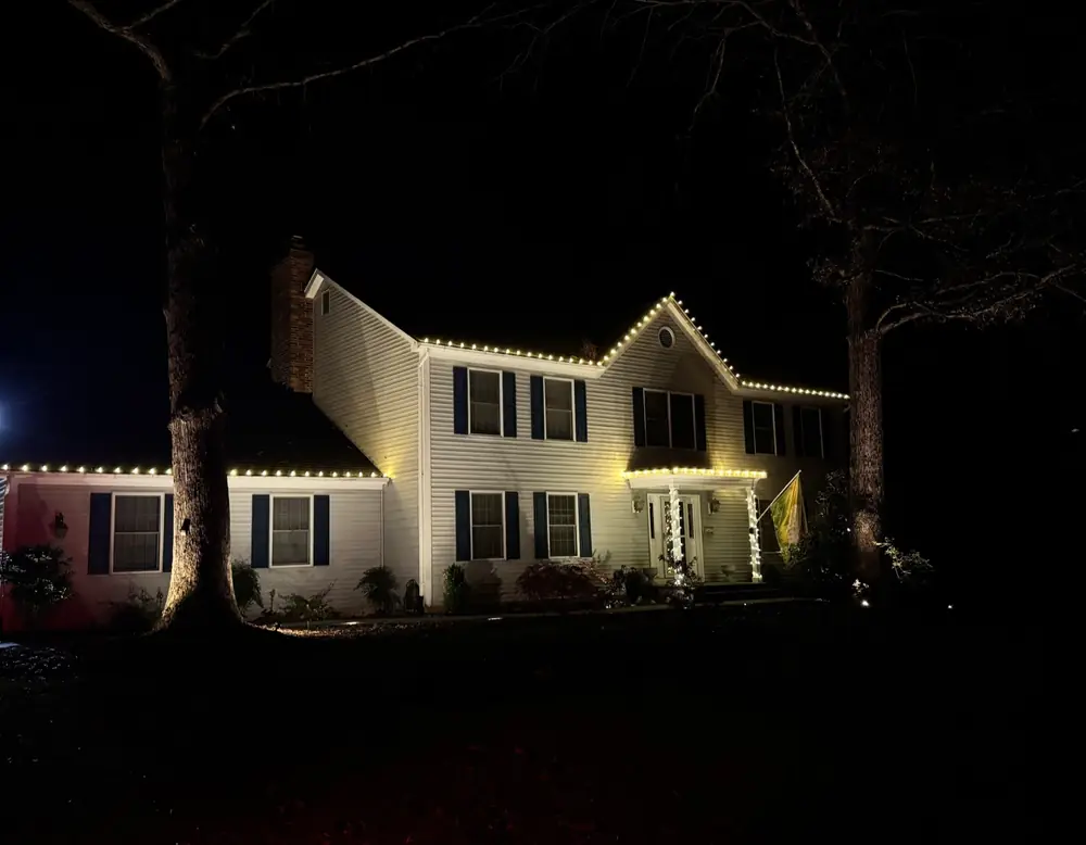 A white house outlined in warm light, seen from the street