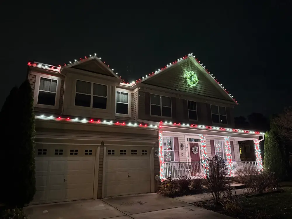 A two-story home with a red and white roofline and a lit green wreath