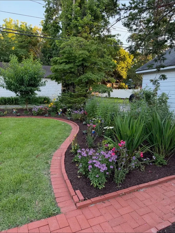 A brick-edged flower bed in bloom beside a mown lawn