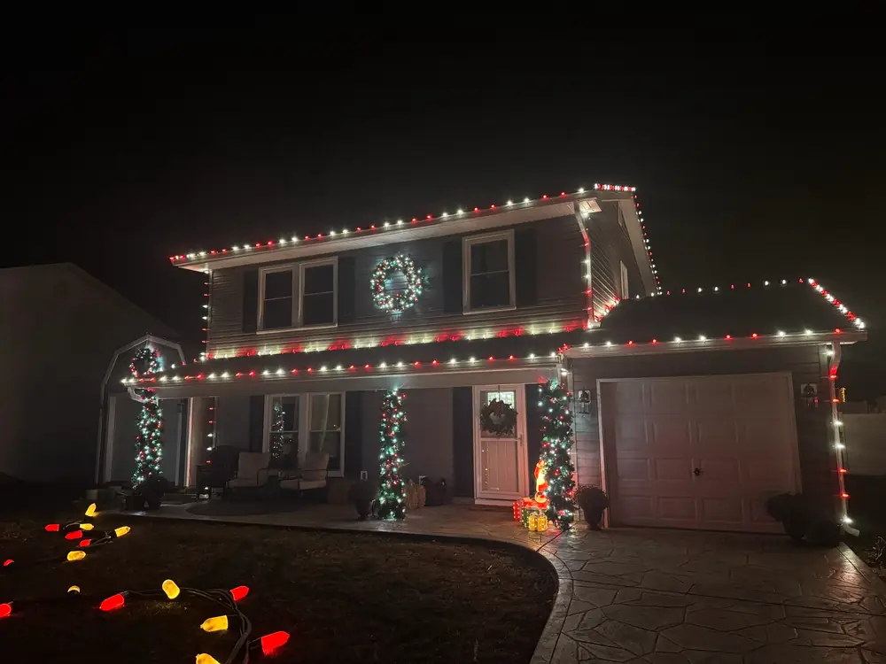 A home with red and white roofline lights and lit wreaths