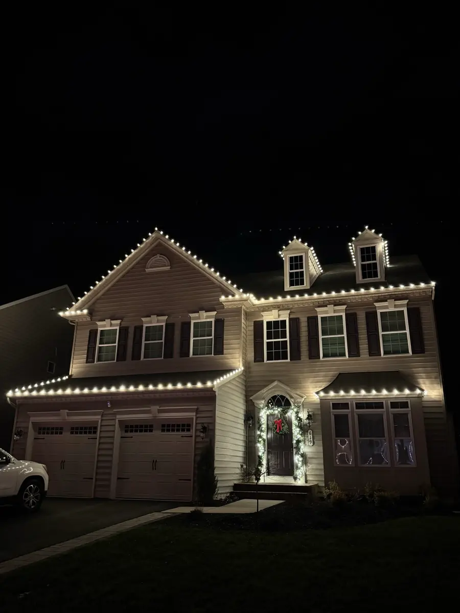 A tan two-story home at night with warm white lights on every roofline