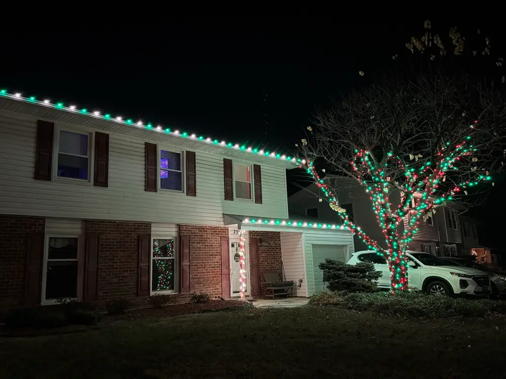 Red, green and white lights on a roofline and a tree
