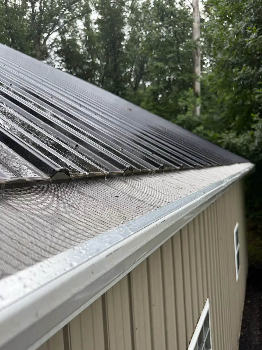 A mesh gutter guard along the edge of a metal roof, wet with rain